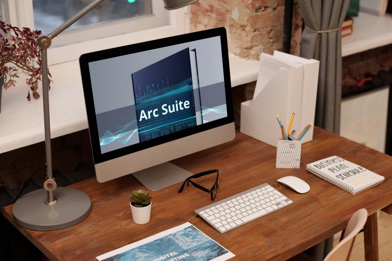 Computer monitor displaying 'Arc Suite' on a wooden desk with office supplies.