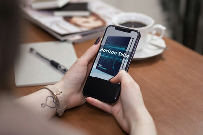 Person holding a smartphone with 'Horizon Suite' app on a desk with coffee and documents.
