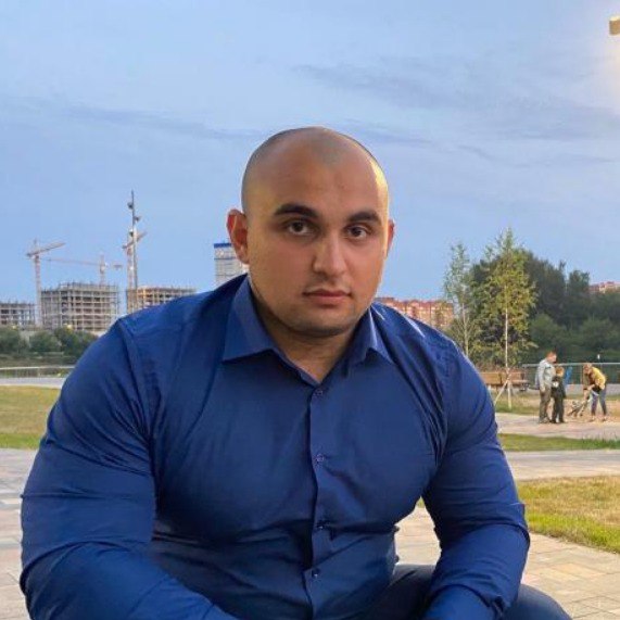 Man in a blue shirt sitting outdoors with construction cranes in the background