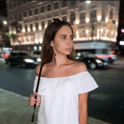 Woman in a white off-shoulder top standing on a city street at night.